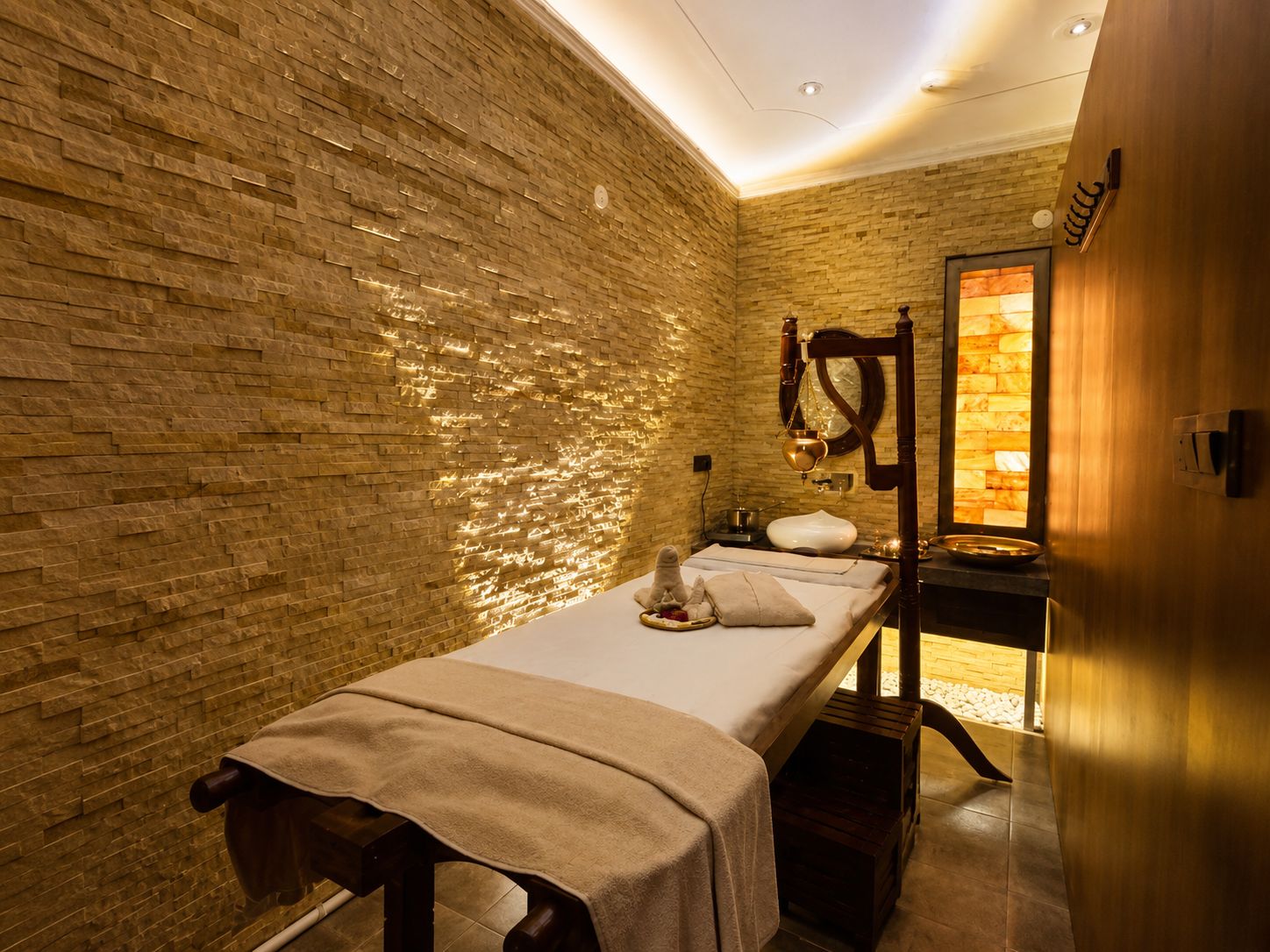 A massage room with a brick wall, a wooden bench, a massage table, and a small window.