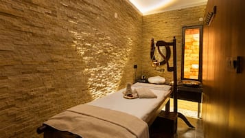A massage room with a brick wall, a wooden bench, a massage table, and a small window.