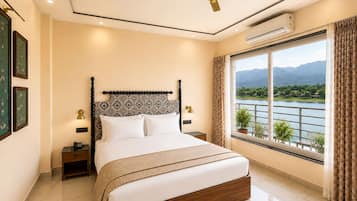 Ein Schlafzimmer mit Bett, Nachttischlampen, Deckenventilator, Klimaanlage, einem Fenster mit Blick auf einen See und Berge sowie einem Nachttisch mit Telefon.