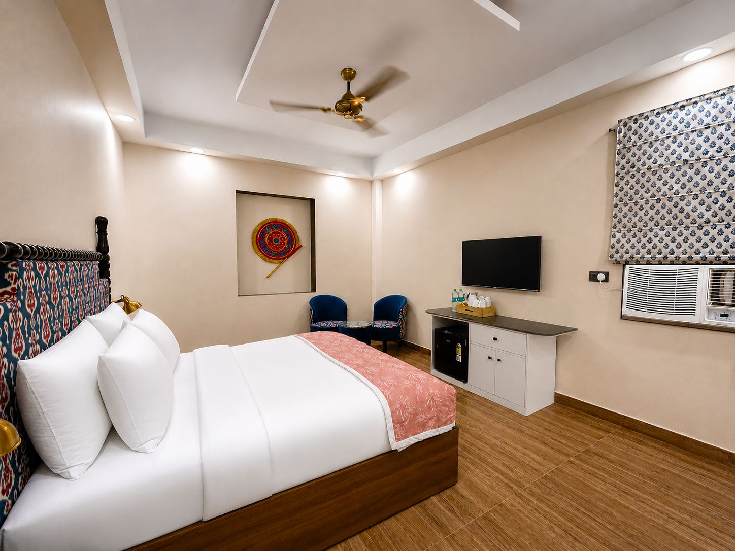 Quarto de hotel com cama, escrivaninha, cadeira, ventoinha no teto, televisão e aparelho de ar condicionado.
