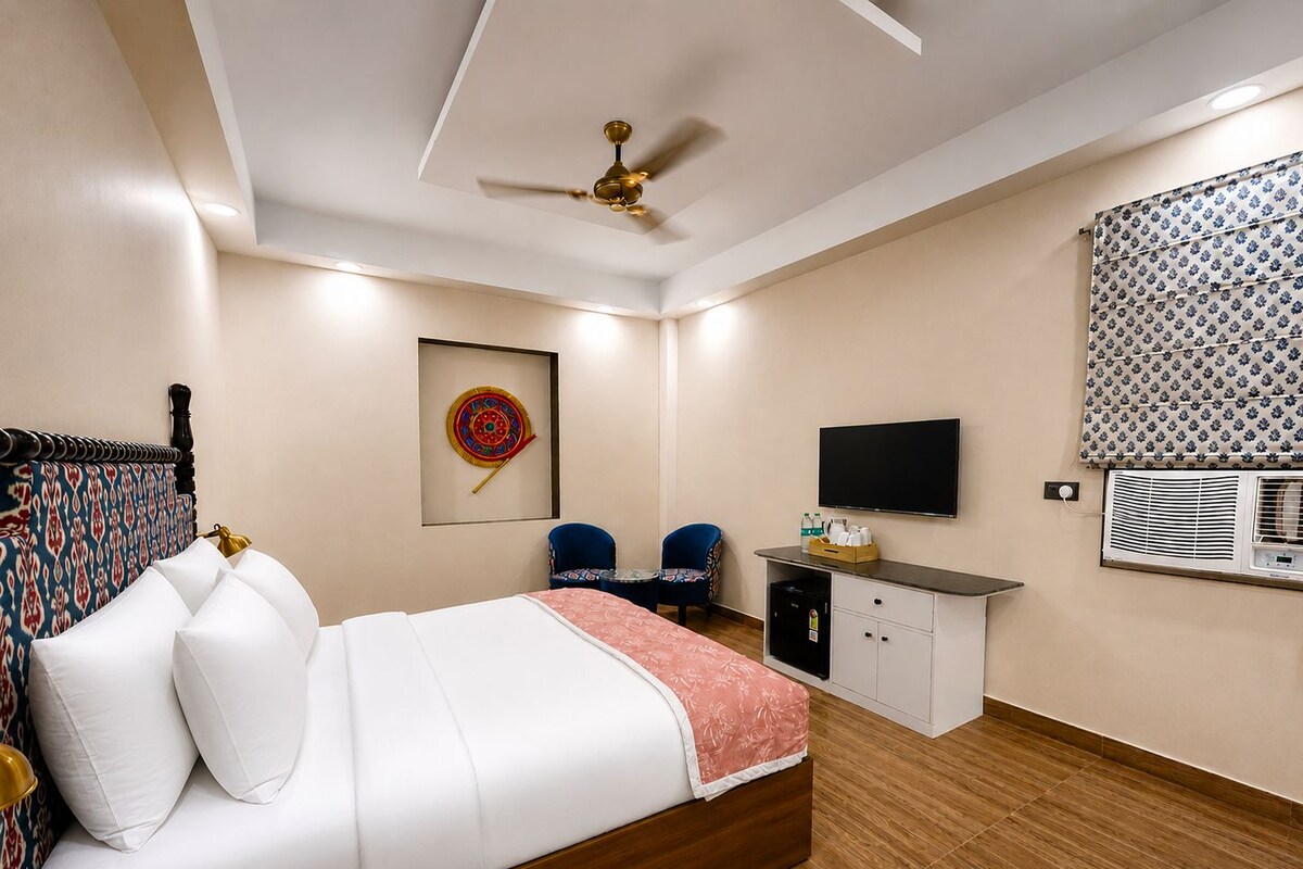 A hotel room with a bed, a desk, a chair, a ceiling fan, a television, and an air conditioning unit.