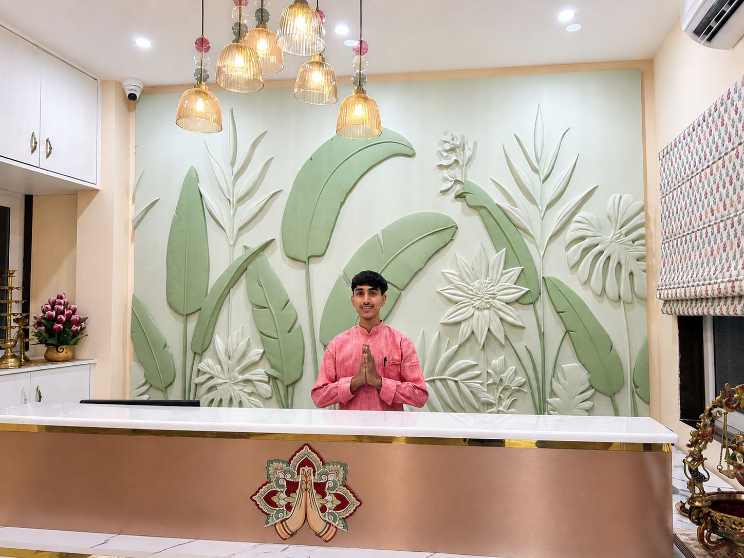 Bancada de recepção com parede decorativa com motivos de plantas, uma pessoa em pé atrás dela e parede estampada à direita.
