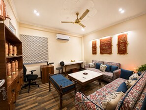 Quarto bem iluminado com ventilador de teto, parede estampada e sofá com almofadas.