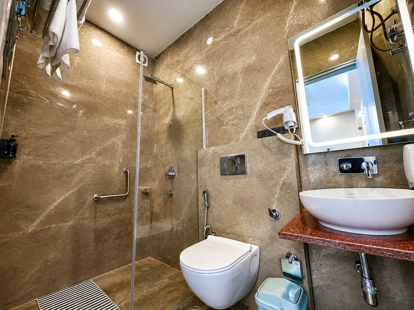 A modern bathroom with a glass-enclosed shower, a white toilet, a sink with a marble countertop, and a mirror with integrated lighting.