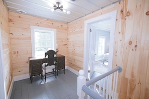 Une pièce aux murs en bois, avec un bureau et une chaise, une fenêtre et une porte donnant sur une autre pièce.