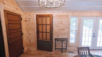 Une pièce aux murs en bois, avec une grande porte en bois, une petite table et une chaise.