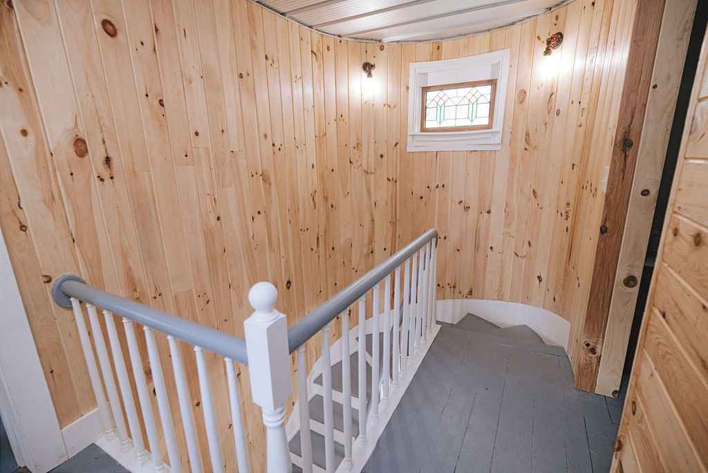 Un intérieur en bois avec une rambarde blanche, une fenêtre au motif géométrique et un plancher en bois.