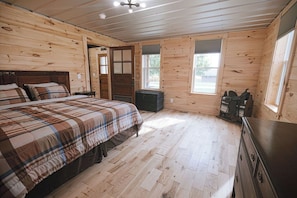 Een slaapkamer in een houten chalet met een bed, een dressoir en een raam.