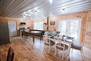 Interior d'una cabana de fusta amb cuina, menjador i una finestra gran.