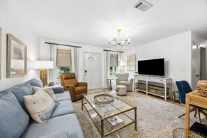 Ein modernes Wohnzimmer mit Sofa, Sesseln, Couchtisch, Fernseher und einem Essbereich mit Tisch und Stühlen.