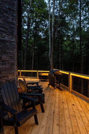 Une terrasse en bois avec des fauteuils Adirondack, un barbecue et un mur en pierre.
