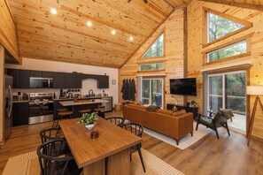 Un intérieur de cabine spacieux comprenant une cuisine, un coin repas et un salon, avec des murs en bois et de grandes fenêtres.