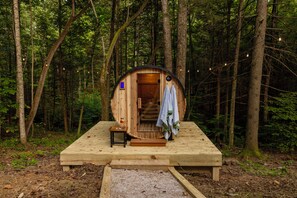 Une cabane en bois avec une porte, une petite table sur laquelle se trouve une bouteille, et un banc.