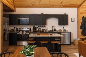 Une cuisine moderne avec des meubles de couleur sombre, des appareils en acier inoxydable et un îlot central doté de tabourets de bar.