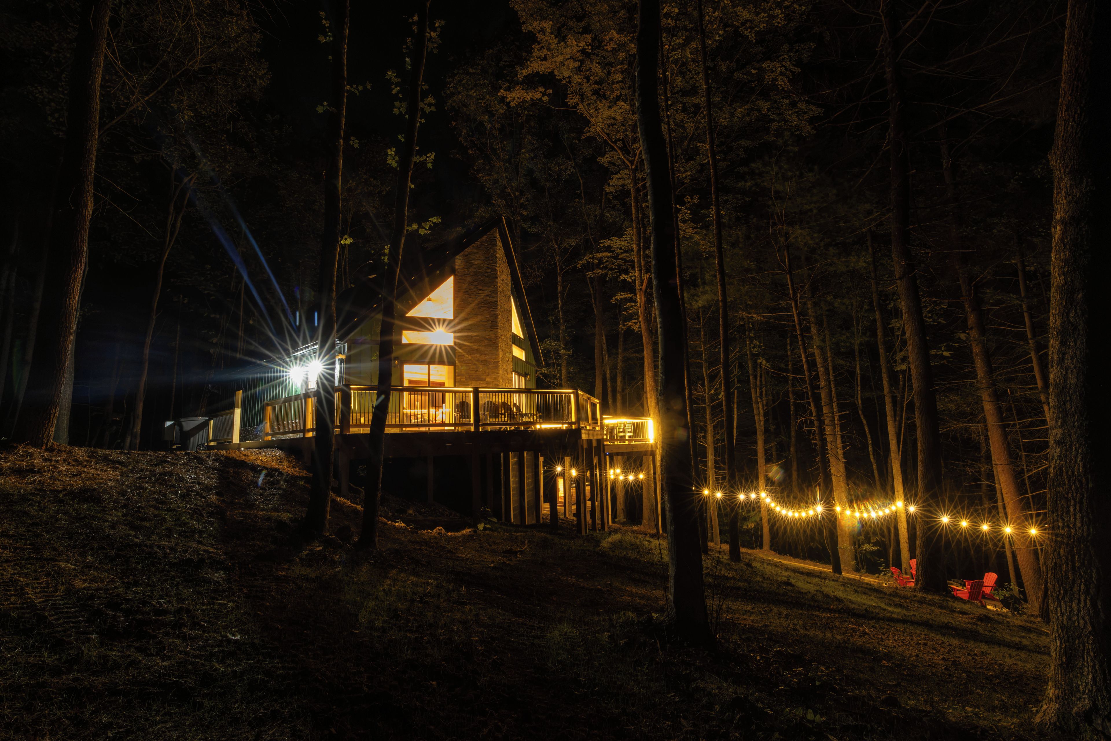 A cabin with a deck, surrounded by trees, at night.