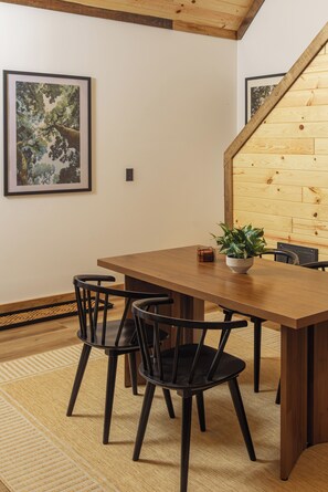 A dining area with a wooden table and chairs, a potted plant, and framed artwork on the wall. - 2 Kings | Hot Tub • Sauna • Firepit • EV • Dogs OK (Zoe)