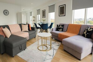 Ein modernes Wohnzimmer mit zwei Sofas, einem runden Couchtisch und einem Essbereich mit Tisch und Stühlen.