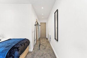 A narrow hallway with a bed on the left, a coat rack in the center, and a door at the end. - Stylish Abodes in Leeds - Sleeps 18 (Leeds)