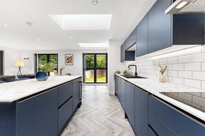 A modern kitchen with dark cabinets, a marble countertop, and a herringbone floor. - Stylish Abodes in Leeds - Sleeps 18 (Leeds)
