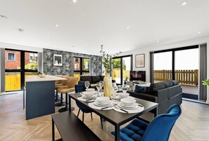 A modern dining area with a table set for four, a sofa, and a view of a balcony. - Stylish Abodes in Leeds - Sleeps 18 (Leeds)
