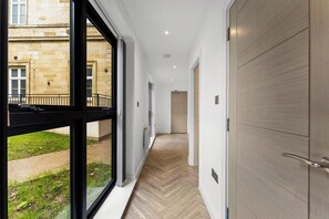 Un pasillo con piso de madera, vista de un edificio exterior y una puerta a la derecha.