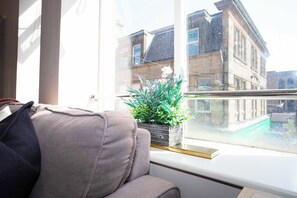 Una habitación con ventana que da a un edificio, un sofá y una planta en maceta sobre el alféizar.