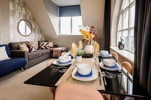 Ein Essbereich mit Tisch für vier Personen, einer Couch und einer dekorativen Vase mit Blumen.