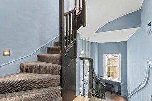 A staircase with carpeted steps and a black handrail leading to a landing with a window. - The Bath Grand | Stylish City Centre Stay for 25 (Bath)