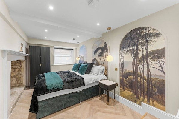 Una camera da letto con un letto, un comodino, un quadro, una finestra e un camino.