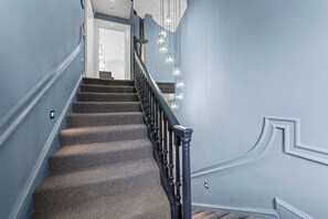 Una escalera con alfombra, barandilla negra e iluminación empotrada en la pared.