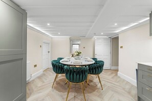 Een eethoek met een ronde tafel gedekt voor zes personen, omringd door vier groene fauteuils met gouden poten.