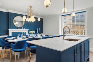 A modern kitchen with a marble island, blue chairs, and pendant lighting. - The Bath Grand | Stylish City Centre Stay for 25 (Bath)