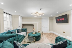 A living room with a green sofa set, a glass coffee table, and a fireplace. - The Bath Grand | Stylish City Centre Stay for 25 (Bath)
