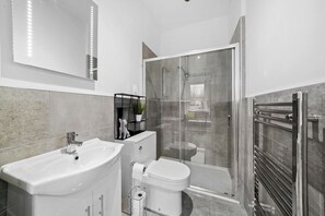 Un bany modern amb plat de dutxa de vidre, un lavabo blanc i un vàter.