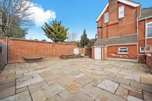 A brick house with a stone patio, a wooden bench, and a tree. - Boutique Maidstone Gem - Sleeps 3 (Maidstone)