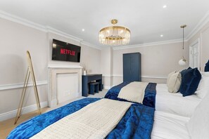 A bedroom with a bed, a television mounted on the wall, a chandelier, and a desk with a chair. - Luxurious Abode in Central Bath (Bath)