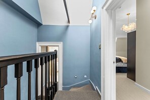 A hallway with a staircase, a door, and a bed in the adjacent room. - Luxurious Abode in Central Bath (Bath)