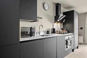 Eine moderne Küche mit grauen Schränken, einer Mikrowelle, einer Kaffeemaschine und einer Uhr an der Wand.
