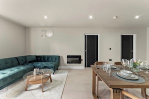 Ein modernes Wohnzimmer mit einem Ecksofa, einem Glastisch, einem Esstisch für vier Personen und einem an der Wand befestigten Flachbildfernseher.