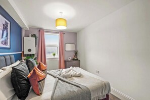 A bedroom with a bed, a bedside table, a lamp, a window with curtains, and a radiator. - Chic Bristol Penthouse - Private Rooftop (Bristol)