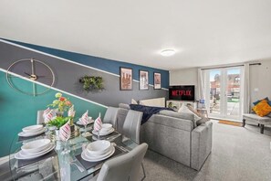 A modern living room with a dining area, a grey sofa, a flat-screen TV, and a view of the outside. - Chic Bristol Penthouse - Private Rooftop (Bristol)