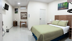 Quarto com cama, mesa de cabeceira, abajur e televisão na parede.