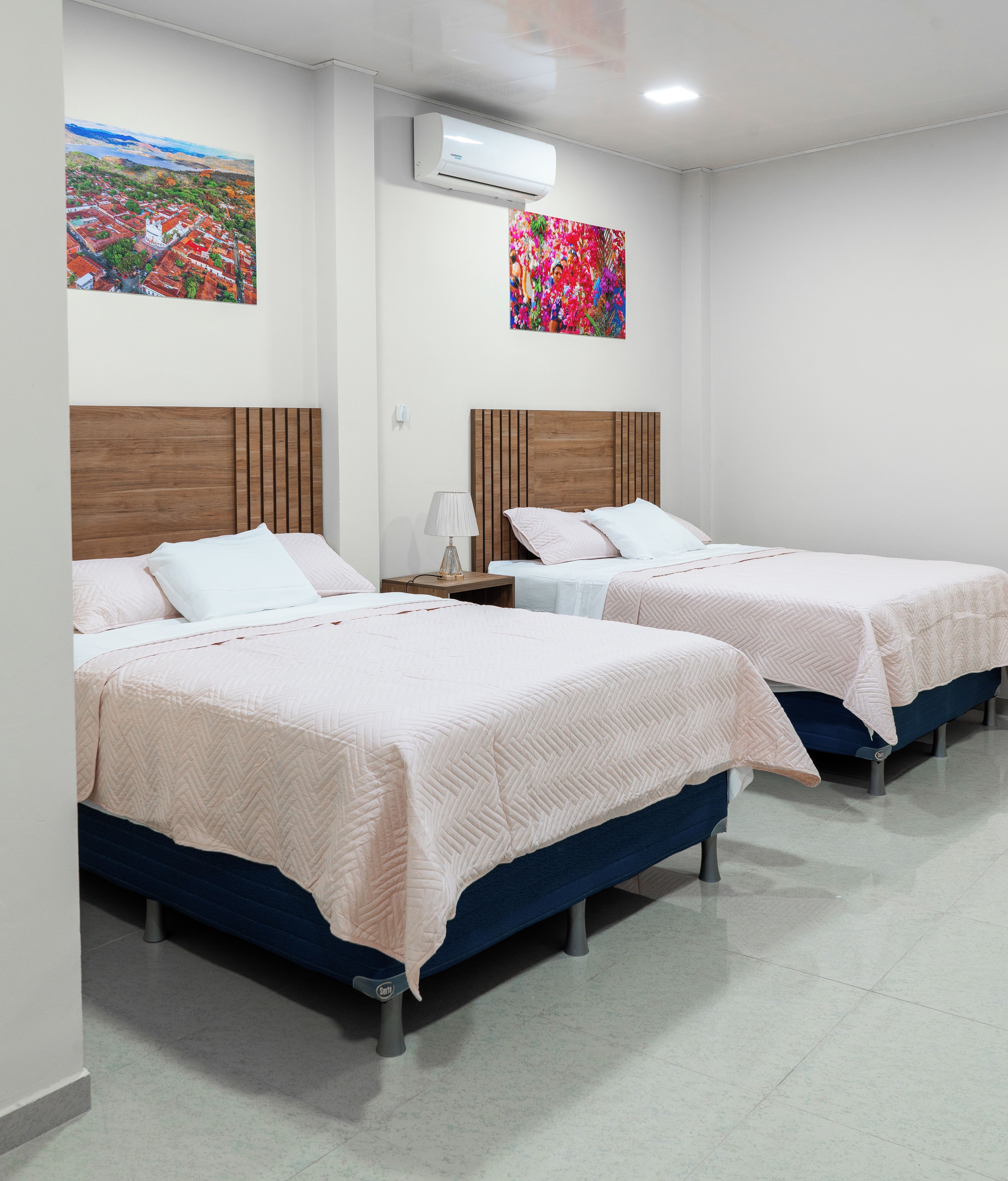 Une chambre d’hôtel avec deux lits, une tête de lit en bois, une table de chevet, une lampe et un climatiseur fixé au mur.