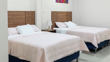 A hotel room with two beds, a wooden headboard, a nightstand, a lamp, and a wall-mounted air conditioner.