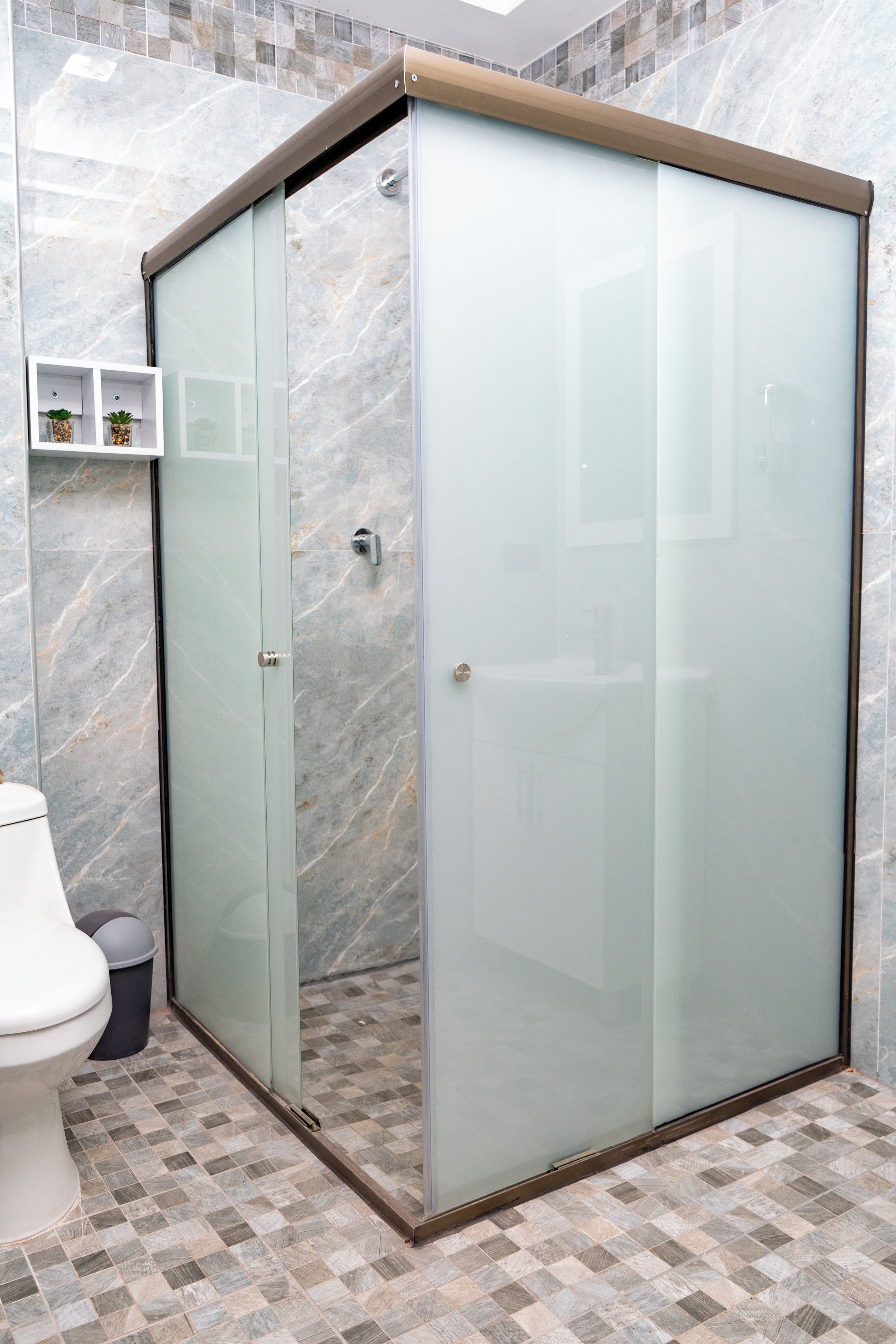 A modern bathroom with a glass-enclosed shower, a toilet, and a trash bin.