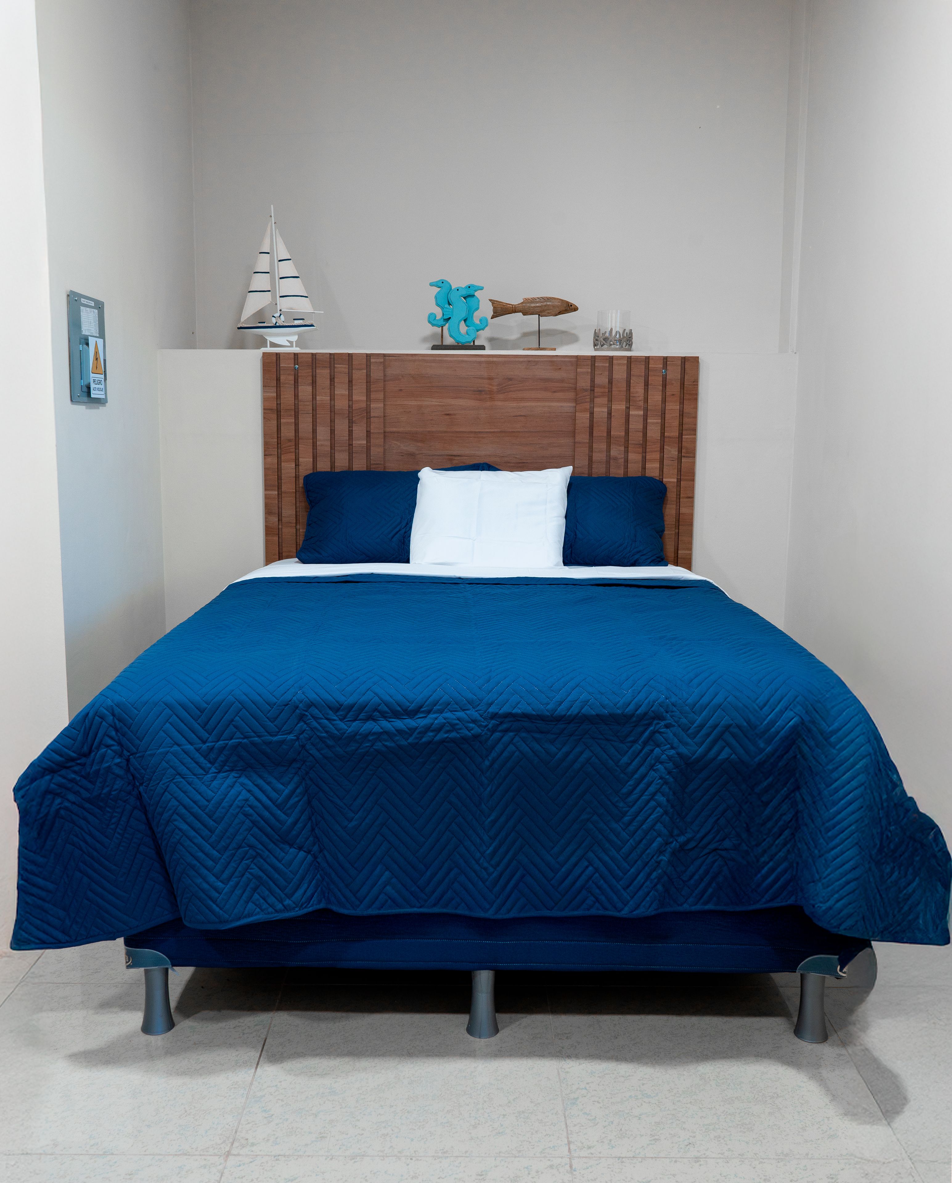 Een bed met een houten hoofdbord, blauw beddengoed en een klein plankje met decoratieve spullen.
