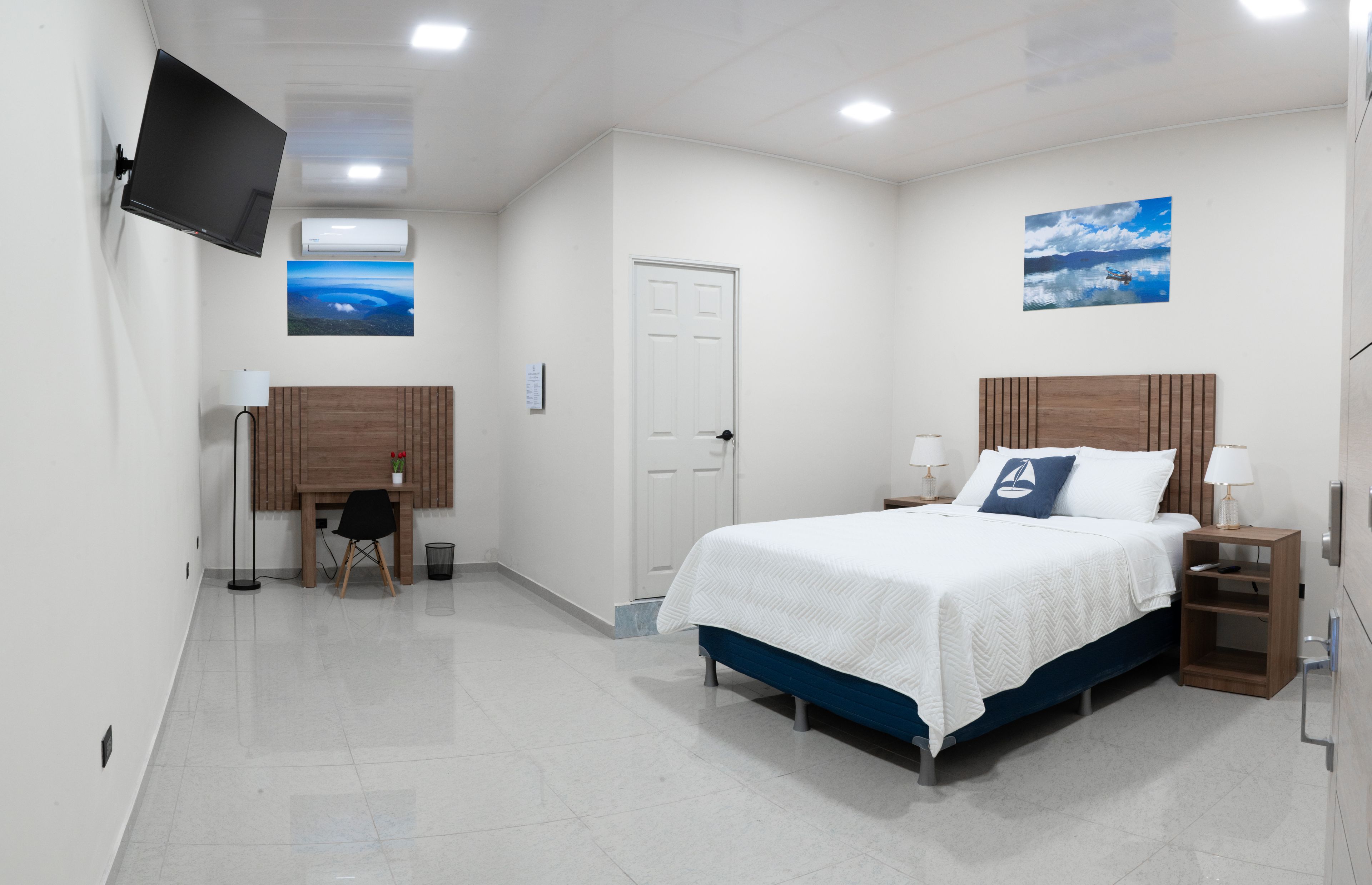 Quarto de hotel com cama, escrivaninha, cadeira, televisão e obras de arte nas paredes.