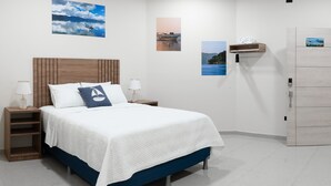 Quarto com cama, mesas de cabeceira, cabeceira de madeira, prateleiras fixadas na parede e obras de arte.