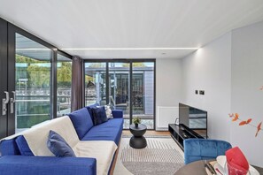 A modern living room with a blue sofa, a black entertainment unit, and a large window offering a view of a building and greenery.