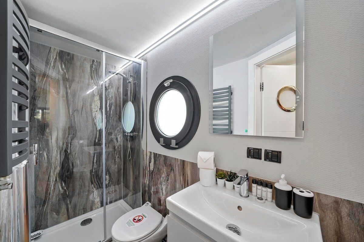 A modern bathroom with a glass-enclosed shower, a toilet, a sink with toiletries, and a mirror with a circular frame.